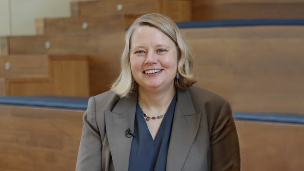 Elinor Karlsson, chief scientist of Darwin's Ark, wears a brown blazer and blue top and sits in a wood-paneled room at the Broad Institute of MIT and Harvard. 